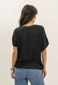 Haut noir à manches courtes avec un col accentué de doré, fabriqué dans un tissu lisse, présentant une coupe décontractée et un design fluide.