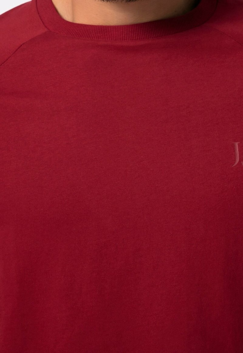T-shirt rossa in cotone con scollo tondo, cuciture visibili e un discreto dettaglio del logo sul petto. Texture liscia, design casual.