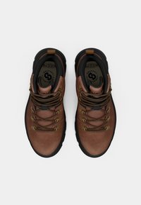 Pruunid nahast matkajalanõud mustade aktsentidega, ümarad varbad ja pronksist detailid. Omab tekstureeritud paelu ja pehmet kaelaosa.