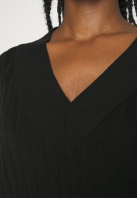 Pull noir côtelé avec un décolleté en V profond et un tissu texturé, mettant en valeur des lignes verticales et une silhouette ajustée.