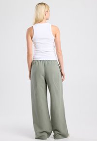 White ribbed tank top paired with relaxed, light green, pinstriped wide-leg trousers. Soft fabric, elastic waistband.