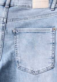 Vaaleansininen farkkukangas, jossa on yksi takatasku suoran muotoilun, näkyvän ommelleen ja pienen metallinen niitin korostuksen kera.