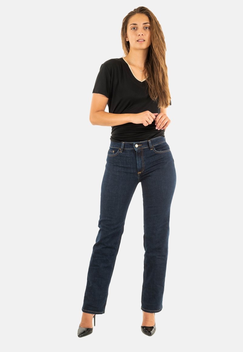 Camiseta negra de cuello en V combinada con jeans de mezclilla azul oscuro de pierna recta. Los jeans cuentan con cinco bolsillos y costuras en contraste. Los tacones negros completan el look.
