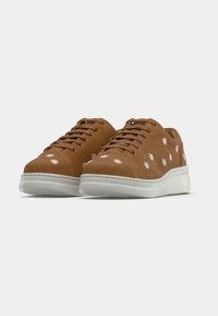 Bruna sneakers i mocka med vit blomsterbroderi, rundad tå och vit gummisula. Snören och sömmar matchar det övre materialet.