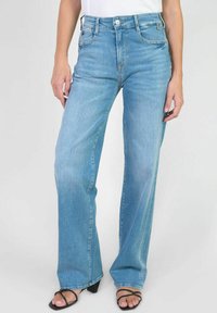 Jean léger en denim bleu, à jambe large et taille haute, avec un délavage clair et une légère décoloration. Il présente un style traditionnel à cinq poches et une fermeture à bouton à l'avant.