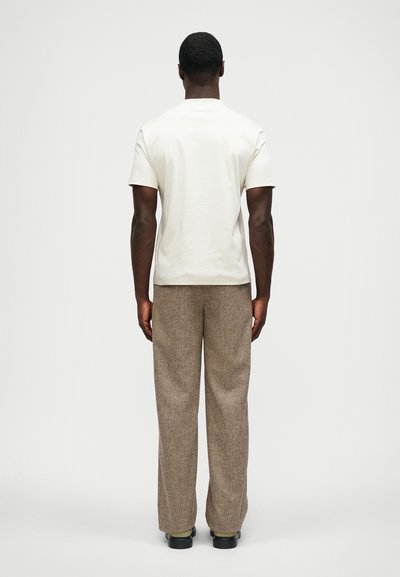 Tricou din bumbac crem și pantaloni largi maro, texturați. Tricoul are mâneci scurte; pantalonii au un model subtil în herringbone.