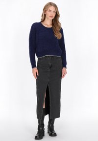 Marineblauwe fluffy trui met een ronde hals en zilveraccenten, gecombineerd met een zwarte dennenrok met een voorknipleef, aangevuld met zwarte laarzen.