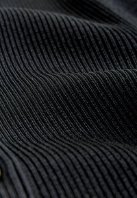 Közelkép fekete bordás szöveten, amelyen emelkedő párhuzamos bordák és puha textúra látható, finom redőkkel.