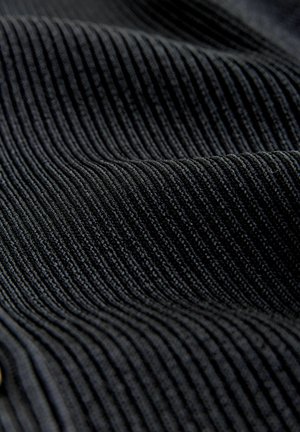 Artimu planu parodytas juodas kordūrinis audinys, kuriame matosi iškilūs lygiagretūs grioveliai ir švelni tekstūra su švelniais raukšlėmis.