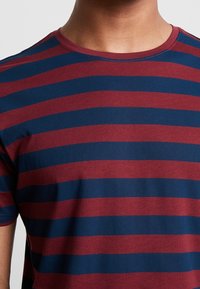T-shirt à rayures rouges et bleu marine avec un col rond. Fabriqué en coton doux, présentant des rayures horizontales uniformément espacées.