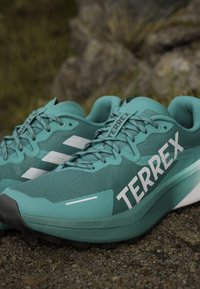 Scarpe da ginnastica teal con tomaia in rete, marchio bianco e imbottitura Lightstrike. Presentano un collare imbottito e suola in gomma testurizzata per una migliore aderenza.