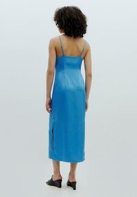 Satin-blaues Midikleid mit dünnen Trägern und einem seitlichen Schlitz, das ein figurbetontes Design und eine glatte Textur aufweist, kombiniert mit schwarzen High-Heel-Mules.