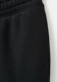 Czarne dresy z miękką fakturą, elastycznym pasem i detalami przy bocznym szwie. Tkanina wydaje się gładka z matowym wykończeniem.