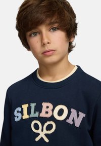 Sudadera azul marino con cuello redondo, que presenta "SILBON" en letras multicolores bordadas y un gráfico de tijeras. Material de algodón, textura suave.