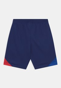 Merkin urheilushortsit, joissa on sileä pinta, ja jotka sisältävät punaisia ja sinisiä kolmiomaisia yksityiskohtia alhaalla. Joustava vyötärö, joka takaa hyvän istuvuuden.