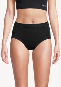 Donna che indossa una biancheria intima nera a vita alta e un crop top nero con un logo visibile su uno sfondo bianco.