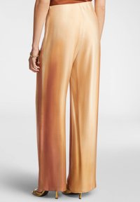 Pantaloni palazzo in satin con una sfumatura che va dal pesco chiaro al rame, caratterizzati da una texture liscia e lucida e una silhouette dritta.
