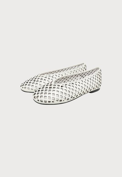 Paire de chaussures plates blanches avec un motif découpé géométrique et des bouts ronds sur fond clair uni.