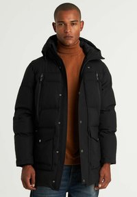 Svart vadderad parka-jacka med dragkedja fram, huva, flera fickor och en glänsande finish, bärs över en brun polotröja.