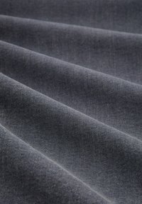 Ciemny materiał dżinsowy o gładkiej fakturze, złożony z warstw tworzących delikatne zagniecenia. Bogaty kolor z subtelnymi wariacjami cieniowania.