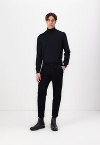 Black turtleneck sweater paired with black pants and black ankle boots. The fabric appears smooth with a fitted silhouette.