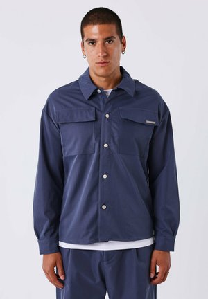 Chaqueta de manga larga color azul marino con un collar clásico, dos bolsillos en el pecho y cierre delantero de botones, fabricada en una tela suave.