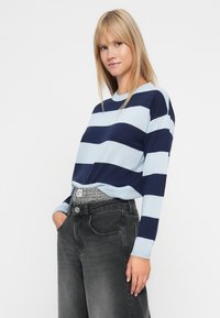 Striped sweater in light blue and navy, featuring long sleeves and a round neckline, paired with dark gray high-waisted jeans.