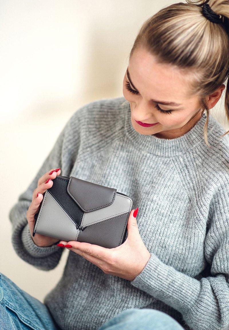 Gray and black leather wallet with a geometric design, featuring a flap closure and zippered compartment, held in hands.