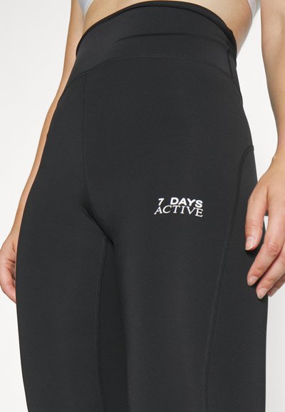 Leggings de sport noirs avec une taille haute, portant le logo brodé « 7 DAYS ACTIVE » en blanc et des coutures plates pour plus de confort.