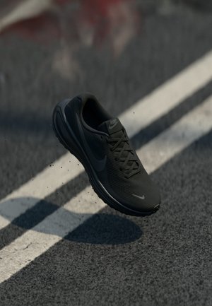 Black Nike athletic shoe with a mesh upper, rounded toe, and textured sole, hovering above a textured surface, with no laces visible.