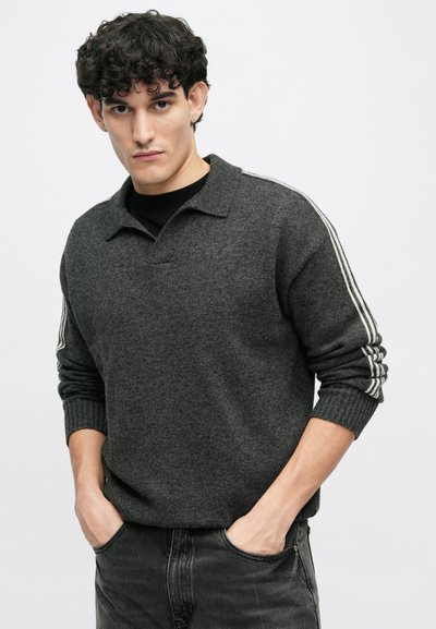 Donkergrijze gebreide pullover met een kraag, voorzien van drie witte strepen op elke mouw en ribgebreide manchetten. Het materiaal lijkt zacht en textuur te hebben.
