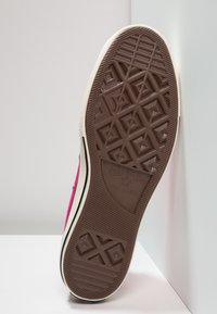 Semelle de sneaker en toile rose avec une base en caoutchouc brun texturé, arborant des motifs géométriques et un logo "Converse All Star".