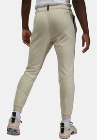 Beiga sportbyxor med en åtsittande design, ribbad textur och svarta sidostråk. Bärs med ljusa sneakers och vita strumpor.