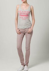 Grå linne med rosa grafik "Hilfiger Denim New York 1985," parat med ljusrosa jeans och vita sneakers. Slät tyg, åtsittande design.