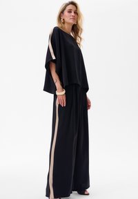 Zwarte wijde broek en een losse zwarte top met beige zijsstripes, gemaakt van een zachte stof en met een ontspannen silhouet.