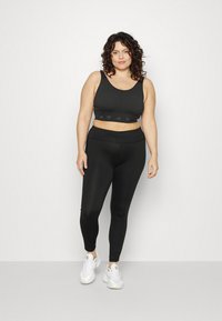 Top desportivo preto com textura canelada, emparelhado com leggings pretas de cintura alta. Ambos têm um design elegante. A modelo usa ténis de atletismo brancos.