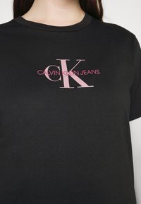 Černé bavlněné tričko s předním potiskem, na kterém je nápis "CK" světle růžovou barvou a pod ním menším růžovým písmem "CALVIN KLEIN JEANS". Krátké rukávy.