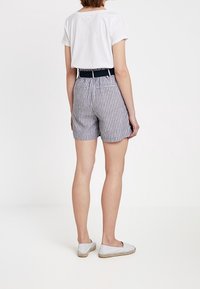 Pruhované šortky s vysokým pasem v modro-bílé barvě, s přiléhavým pasem a postranními kapsami, v kombinaci s obyčejným bílým tričkem a plochými botami.