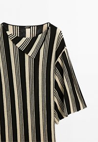 Loose-fitting top with wide short sleeves, black and cream vertical stripes, and an asymmetric collar detail. No visible people.