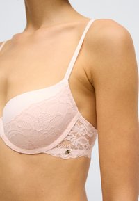 Φωτεινό ροζ σουτιέν με δαντελένιο τελείωμα, λεία κύπελλα, ρυθμιζόμενους ιμάντες και μικρό μεταλλικό διακοσμητικό στη ζώνη.