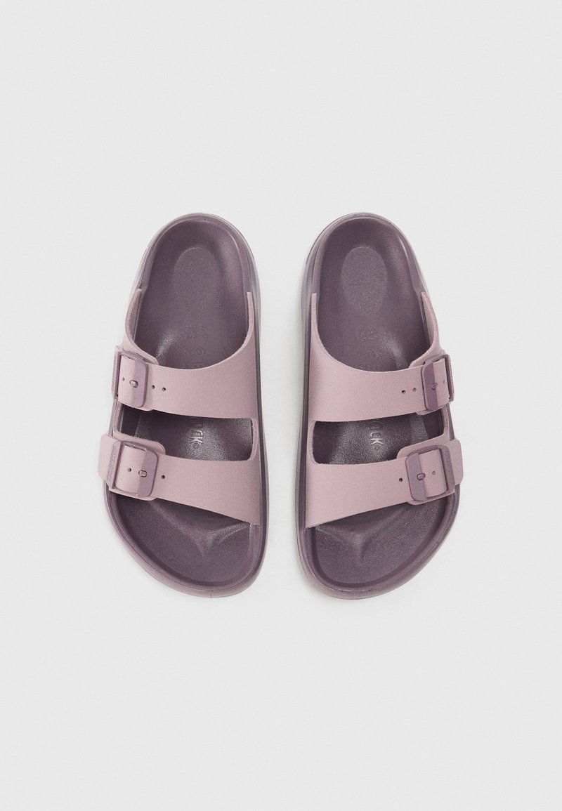 Sandales en plastique violettes avec deux boucles réglables, semelle plate et semelle intérieure texturée, présentant une surface lisse et un design à bout arrondi.