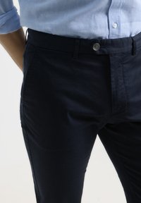 Pantalones de color azul marino con una textura suave, que presentan un diseño clásico, bolsillos frontales y un cierre de botón metálico en la cintura.