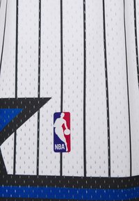 Canotta da basket bianca con strisce verticali nere, dettagli blu e texture in rete traspirante. Presenta il logo NBA nell'angolo in basso.