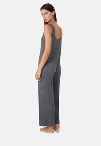 Jumpsuit gris acanalado con piernas anchas y espalda descubierta, hecho de un tejido texturizado. El modelo está descalzo, posando de lado.