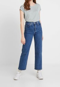 Ljusgrå t-shirt med kort ärm i kombination med högmidjade blå denimjeans, som har en rak bendesign och vita sneakers.