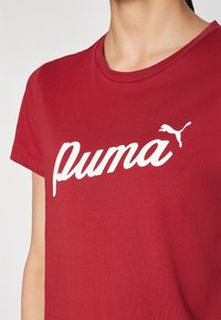 Czerwona bawełniana koszulka z białym, stylizowanym logo "Puma" oraz małym białym sylwetką pumy po lewej stronie. Klasyczny okrągły dekolt.
