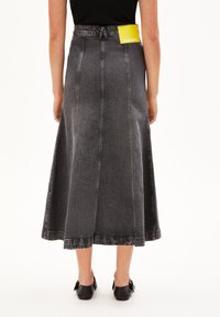 Jupe maxi en denim gris avec des coutures verticales visibles, une légère évasement et une taille. Comprend une étiquette jaune positionnée à l'arrière.