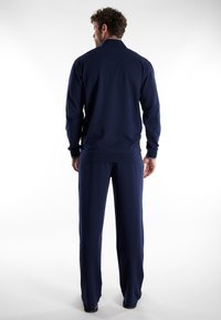 Navyblauw trainingspak met een jack met ritskraag en bijpassende broek. Heeft een gladde textuur en aansluitende manchetten, wat zorgt voor een gestroomlijnde uitstraling.