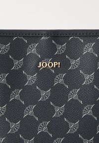 Close-up of a dark blue bag with a textured pattern featuring repeating floral designs, highlighted by a gold "JOOP!" logo.