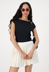 Black short-sleeve top with an asymmetrical neckline paired with a pleated cream skirt. Accessories include pink sunglasses and a black bag.